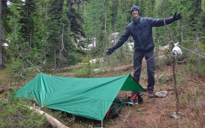 a person stands beside a shelter they made on an outward bound course 